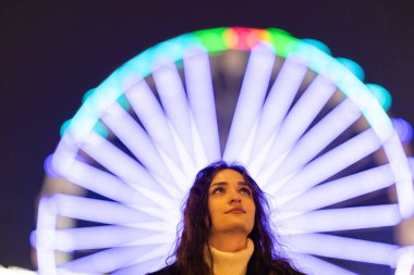 Geceleri arka planda parlayan dönme dolap ışıklarıyla yukarı bakan genç bir kadın.