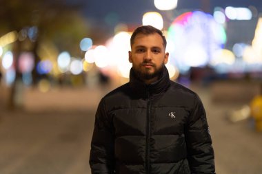 Genç adam gece dışarıda duruyor, soyut, bulanık şehir ışıklarıyla çevrili.