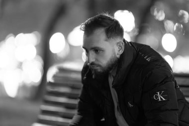 Genç adam bir bankta tek başına oturuyor, geceleyin derin derin bakıyor.