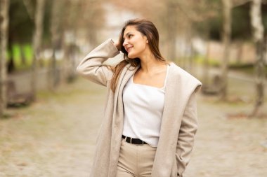 Güzel bir açık hava parkında poz verirken gülümseyen genç bir kadın.