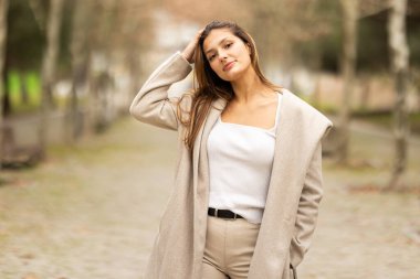 Genç bir kadın kendine güvenerek poz veriyor, saçını dışarıda dikerken düzeltiyor.