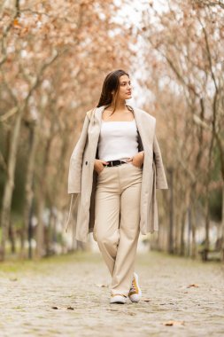 Sonbahar ya da kış aylarında kaldırım taşı patikasında rahatça duran genç bir kadın.