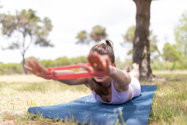 Young woman strengthening her back and core muscles using a resistance band on a mat outdoors