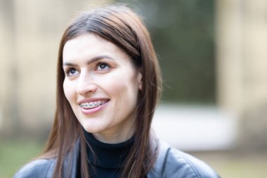 Gülümseyen, diş tellerini gösteren, umut dolu bir ifadeyle yukarı bakan genç bir kadın.