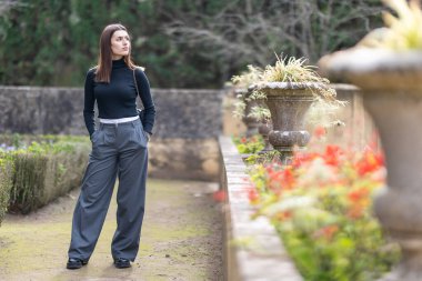 Bahçede rahat bir şekilde duran genç bir kadın. Yaşam tarzı ve keyfi için şık giyinmiş.