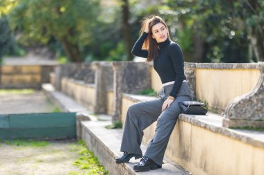 Taş duvarda oturan bir kadın, elleri saçında, dışarı çıkmaktan zevk alıyor.