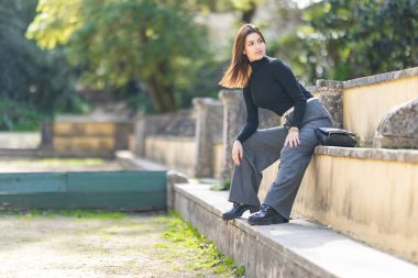 Taş bir çıkıntıda oturan genç bir kadın, güneşli bir günün tadını çıkarıyor.