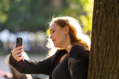 Akıllı telefonu tutan genç bir kadın, açık hava ortamında içerik yaratıyor.