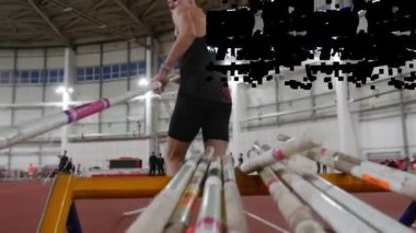 Erkek sporcu, bir spor sahasında sırıkla atlama antrenmanından önce askıdan direk seçiyor.