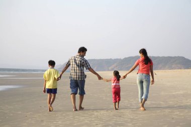 Güney Asyalı ebeveynler ve çocuklar deniz kıyısında el ele yürüyorlar, Shiroda, Dist Sindhudurga, Maharashtra, Hindistan 