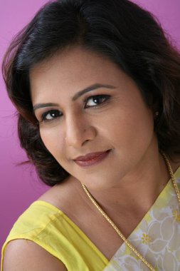 Sarı sari giyen ve kameraya bakan Güney Asyalı genç bayan. 