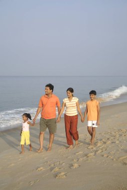 Güney Asyalı ebeveynler ve çocuklar deniz kıyısında el ele yürüyorlar, Shiroda, Dist Sindhudurga, Maharashtra, Hindistan