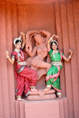 Women performing classical traditional Odissi dance at statue on stage  clipart