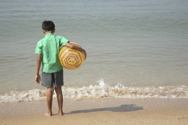 Güney Asyalı Hintli çocuk deniz kıyısında renkli plastik hava topunu koluyla bel arasında tutuyor.