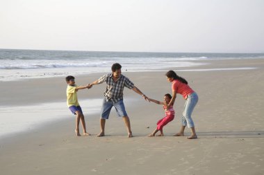 Güney Asyalı ebeveynler ve çocuklar deniz kıyısında birbirini çekme oyunu oynuyorlar, Shiroda, Dist Sindhudurga, Maharashtra, Hindistan