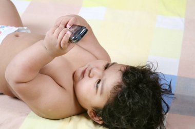 Bir buçuk yaşında bir bebek sırt üstü uyuyor ve cep telefonuna bakıyor.