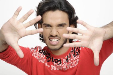 Genç çocuk avuçlarını önünde gösteriyor. Parmakları açık, dişlerini gösteriyor. 