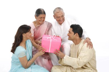 Genç bir kadın ve bir adam ellerinde hediye kutusuyla yaşlı bir aileye veriyorlar. 