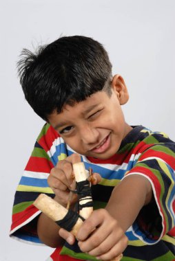 South Asian Indian boy aiming catapult at camera over white studio background clipart