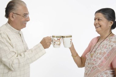 Ellerinde çay ya da kahve fincanları tutan yaşlı mutlu çiftin birbirlerine dokunması ve gülümsemeleri. 