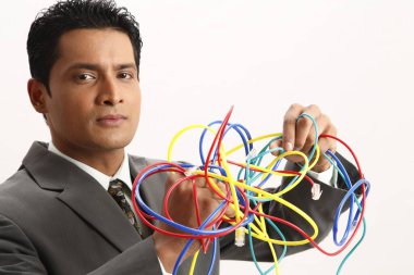 Bir grup renkli kabloyu tutan bir iş adamı iki eliyle onları birbirinden kurtarmaya çalışıyor.