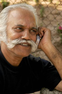 Bahçede cep telefonuyla konuşan yaşlı bir beyefendi. 