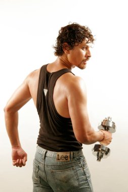 South Asian Indian man wearing black vest and curly oily hair building arms muscles with steel dumbbell clipart