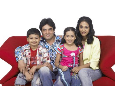 Güney Asyalı aile, baba, anne, oğul ve kız kanepede oturmuş kameraya bakıyorlar. 