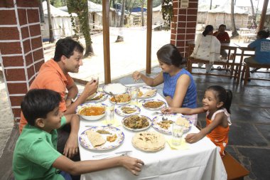 South Asian Indian parents and children taking lunch on dining table in resort , Shiroda , Dist Sindhudurga, Maharashtra , India  clipart