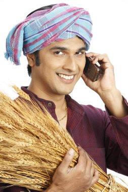 Rich Indian farmer holding harvested golden wheat crops and talking on mobile  clipart