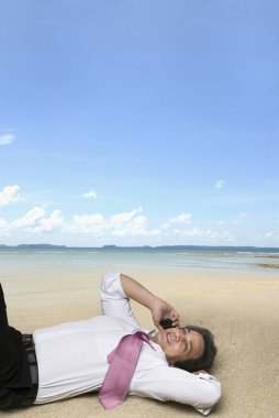 Yönetici deniz kıyısındaki kumda rahatlarken cep telefonuyla konuşuyor.