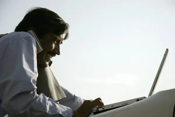 stock image Indian businessman wearing light blue shirt and tie using laptop on bonnet of car and talking on mobile phone Pune , Maharashtra , India 