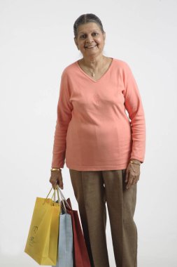 Sağ elinde renkli alışveriş torbaları tutan yaşlı kadın. 