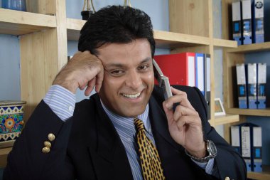 Yönetici sağ yumruğuyla dinleniyor ve cep telefonuyla konuşuyor. Kabinde duruyor.