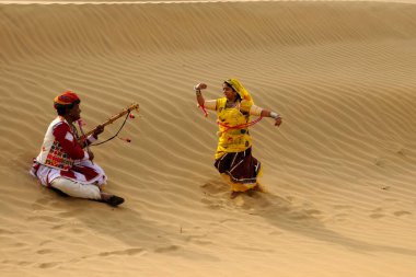 Halk müziği çalan ve kum tepelerinde dans eden bir çift, Jaisalmer, Rajasthan, Hindistan 