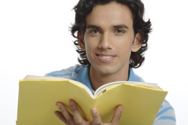 Yüzünün önünde sarı kaplı kitap tutan ergen çocuk. 