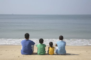 South Asian Indian parents and children facing Arabian Sea sitting on seashore, Shiroda , Dist Sindhudurga, Maharashtra, India   clipart