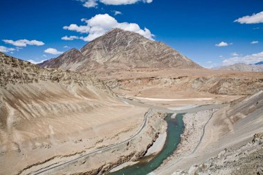 İndus nehrinin yeşil suları ve Zanskar nehrinin çamurlu kahverengi suları ve arka planda kısır Ladakh manzarası, Ladakh, Jammu ve Kashmir, Hindistan 