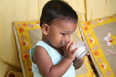 Güney Asyalı küçük bir çocuk. 1 yaşında. Tek başına süt içiyor.