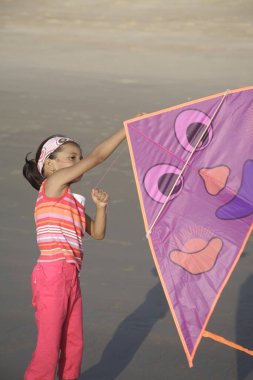 Güney Asyalı kız deniz kıyısında renkli uçurtma uçurmaya çalışıyor.