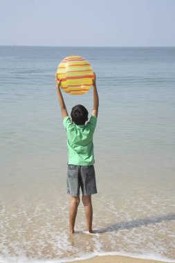 Güney Asyalı çocuk deniz kıyısında renkli plastik hava topuyla ayakta duruyor.