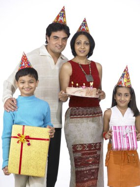 Güney Asyalı aile, baba, anne ve kız paketler ve doğum günü pastası taşıyorlar.