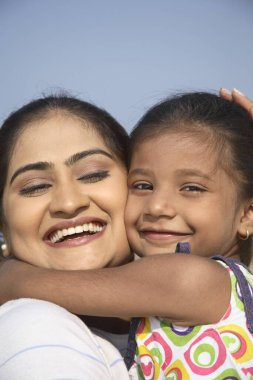Güney Asyalı Hintli kız annesinin kucağında oturmuş sahilde birbirlerine sarılıyorlar.