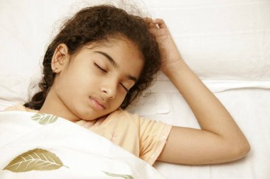 South Asian Indian 9 years old girl wearing peach colour nightwear having sound asleep on bed clipart