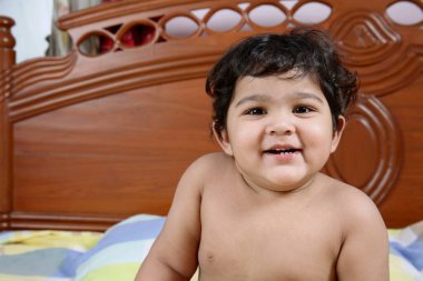 Bir buçuk yaşında bebek yatakta oturuyor ve gülümsüyor. 