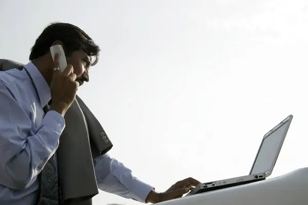 stock image Indian businessman wearing light blue shirt and tie using laptop on bonnet on car and talking on mobile Pune , Maharashtra , India