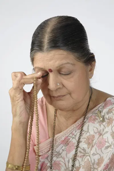 Stock image Old lady praying with rosary or japmala in her right hand touching to right eye 