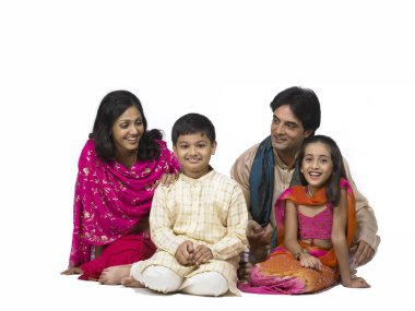 Güney Asyalı ailede baba, anne, oğul ve kız gülümseyip kameraya bakıyorlar. 