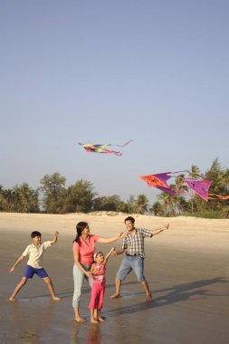 Güney Asyalı ebeveynler ve çocuklar deniz kıyısında renkli uçurtmaları uçurmaya çalışıyorlar, Shiroda, Dist Sindhudurga, Maharashtra, Hindistan 