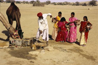 Rajasthani kuyudan su çeken adam ve bekleyen kızlar, Khuhri, Jaisalmer, Rajasthan, Hindistan 
